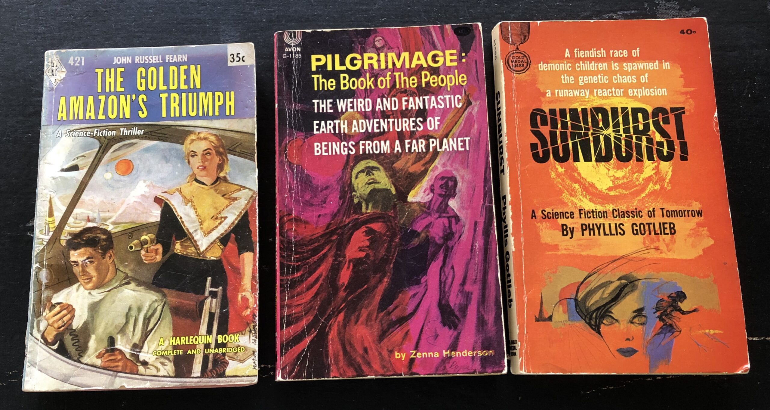 From left to right: The Golden Amazon’s Triumph  by John Russell Fearn, 1958, Harlequin Books, cover art uncredited; Pilgrimage: The Book of the People by Zenna Henderson, 1961, Avon reprint of Doubleday hardcover, cover art uncredited; and Sunburst by Phyllis Gotlieb, 1964, Fawcett Gold Medal original (developed from shorter version published in Amazing Magazine), cover art uncredited. Photo by Rosemary Jones, from the author’s collection.