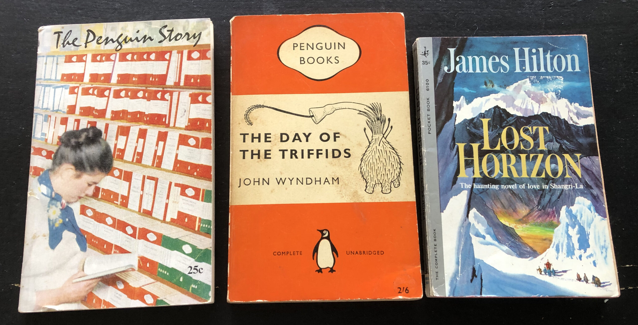 From left to right: The Penguin Story, 1956, with cover photo by Guy Gavett showing Penguin rack at W. H. Smith & Son; The Day of the Triffids by John Wyndham, 1960 edition with small black-and-white cover art added to white band; and Lost Horizon by James Hilton, 1961 (#6100 47th printing), Pocket Books, cover art uncredited. Photo by Rosemary Jones, from the author’s collection.